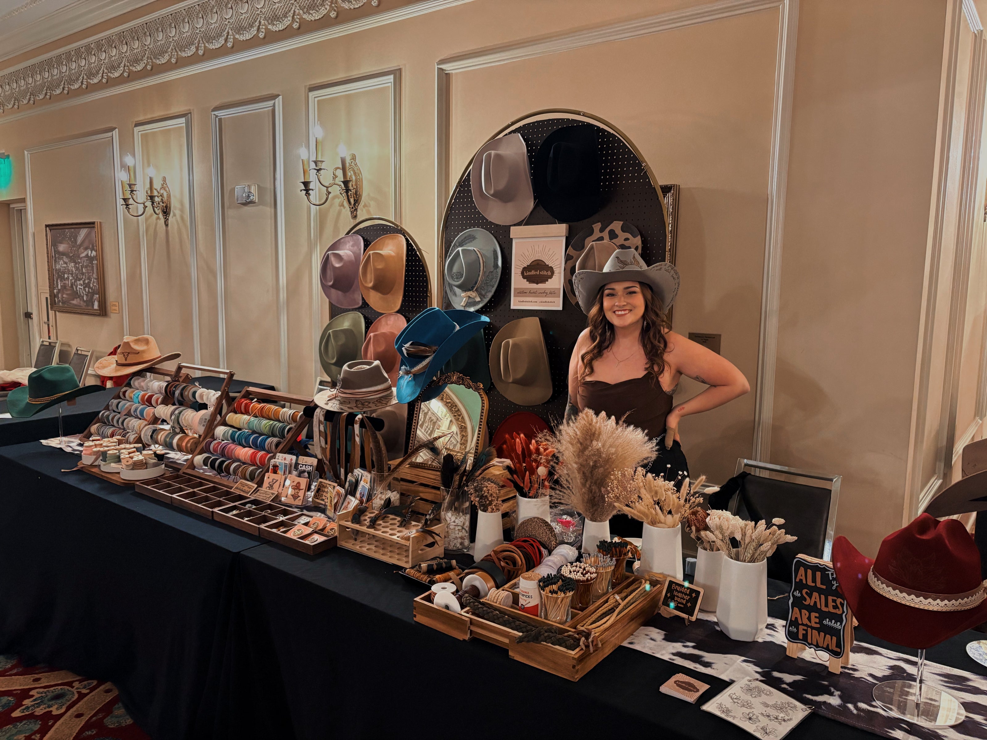 Rachel (Owner of Kindled Stitch) standing behind a table displaying various hats and accessories at Fashion Week Spokane's 2025 Fall Runway.